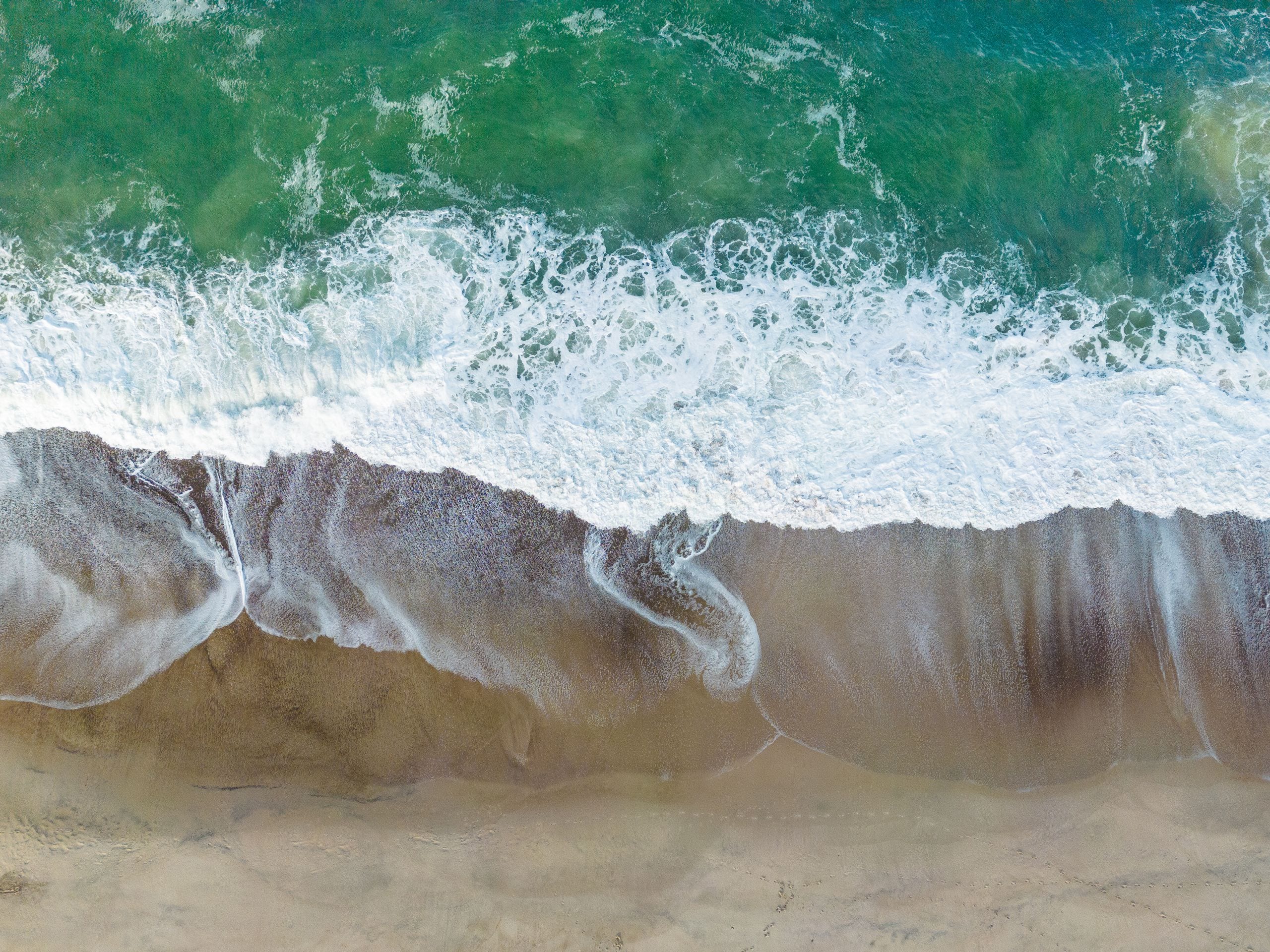 Aerial shot of waves crashing onto the sandy shores of Thisted beach,