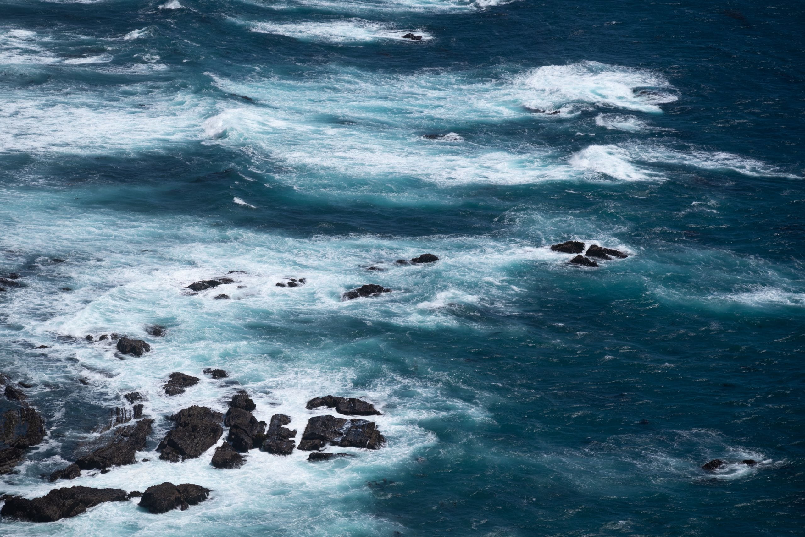 Dynamic aerial shot of the Pacific Ocean waves crashing over rocks in