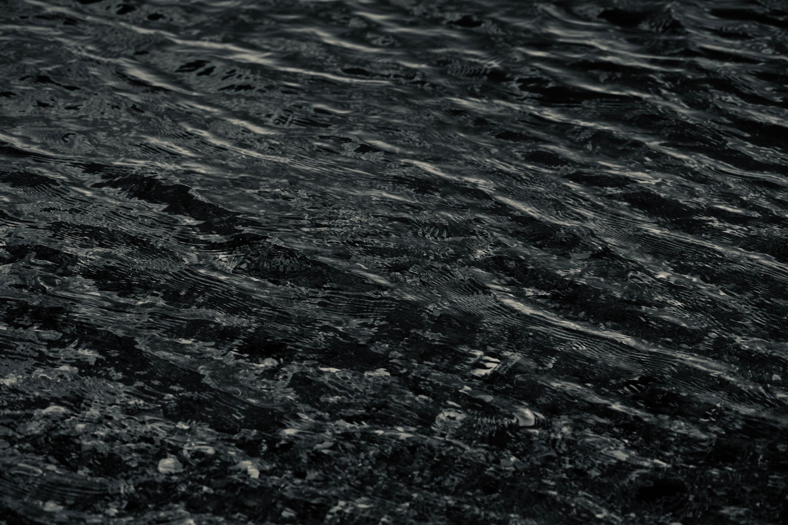 A moody close-up of dark wavy water texture, showcasing natural patter