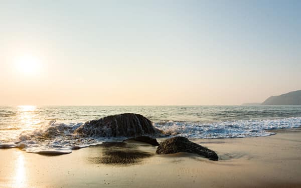 Peaceful beach view with rocks and gentle waves under a warm sunset sk
