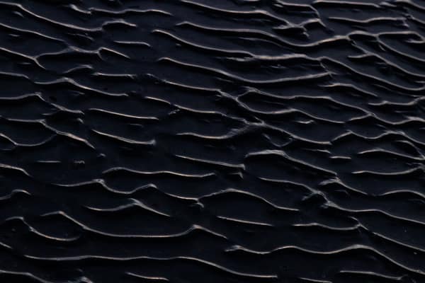 Close-up view of dark sand ripples creating a unique abstract texture 