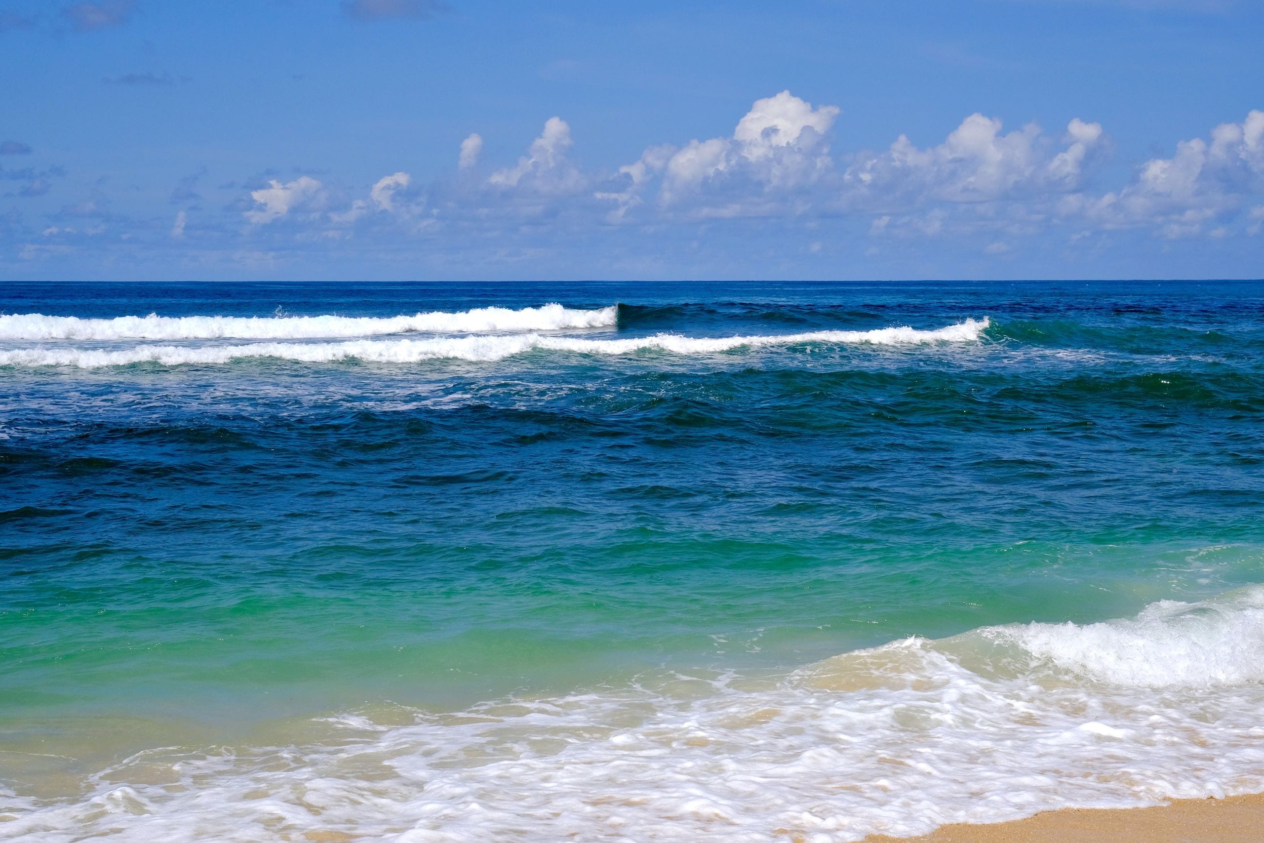 Bright blue ocean waves gently crashing on a sandy shore under a clear