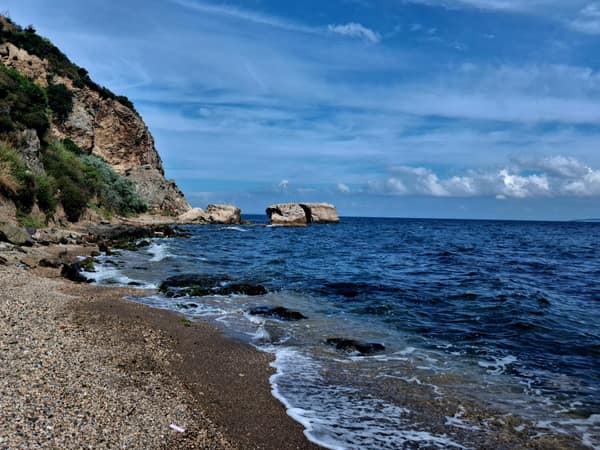 Tranquil beach scene with rocky cliffs and clear blue water under a vi