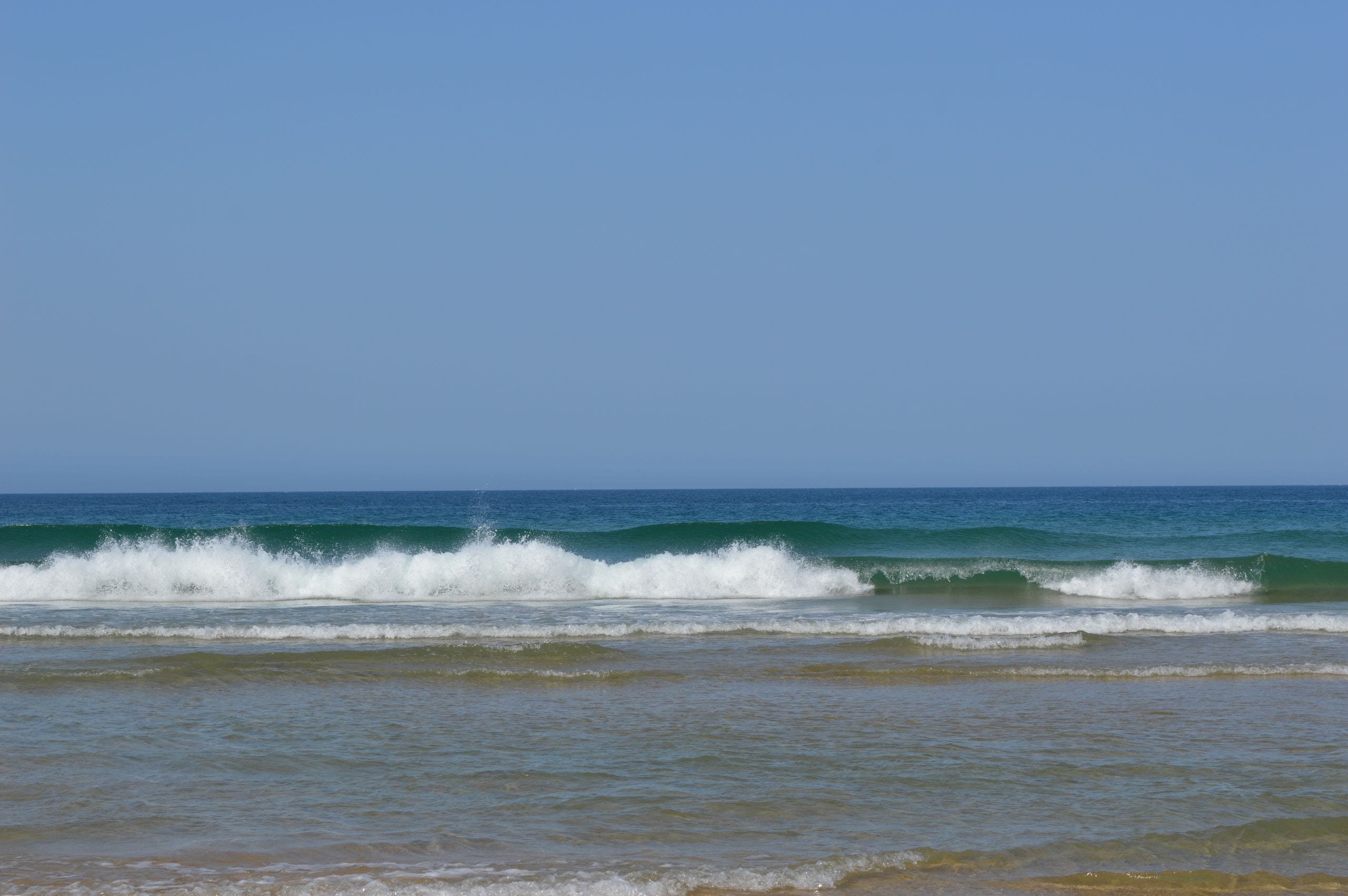 Calm ocean waves gently crashing on a sandy beach under a clear blue s