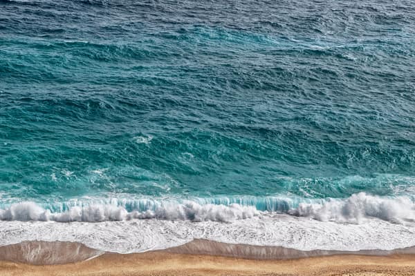 Dynamic ocean waves crash onto a sandy shore, showcasing the beauty of