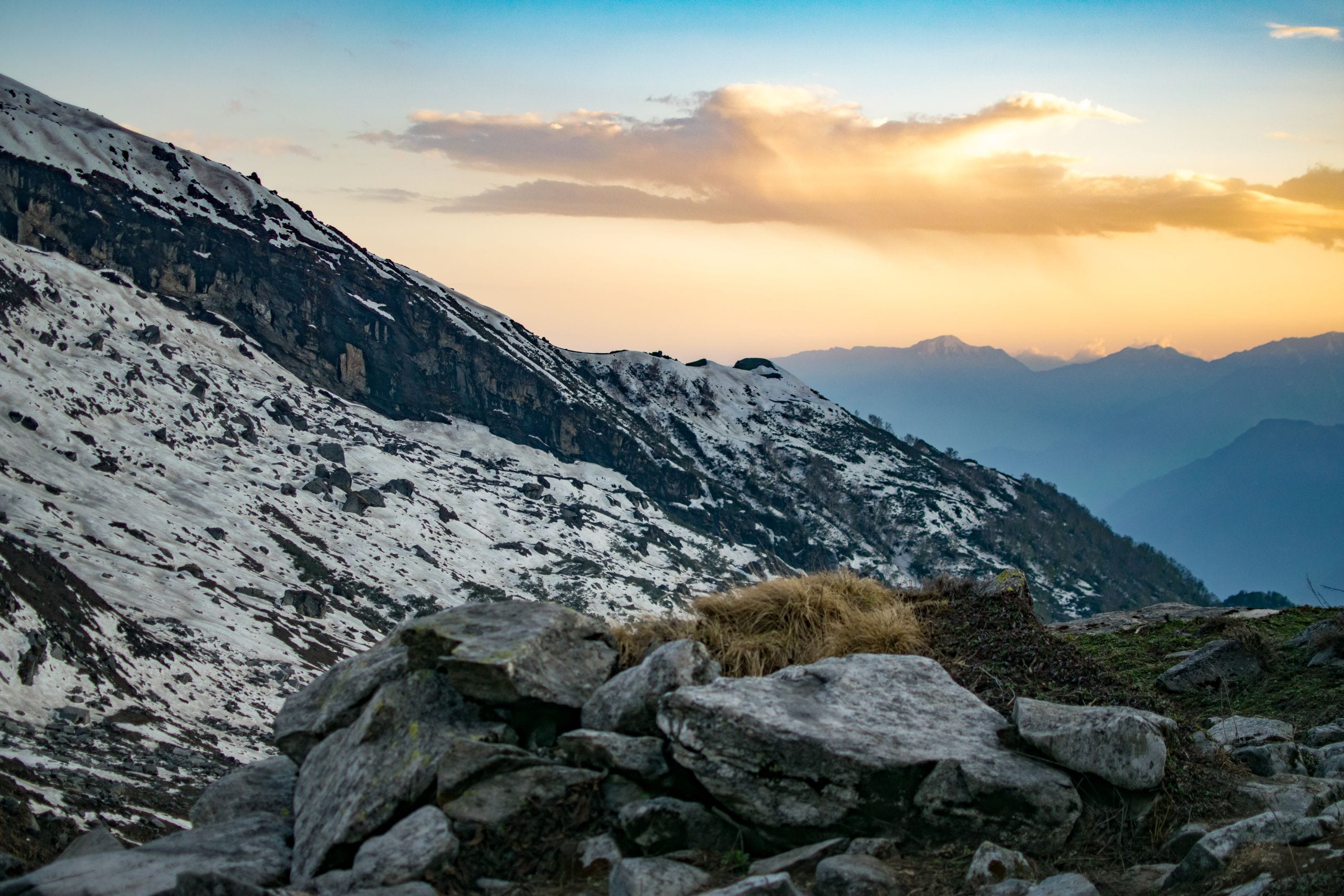 Snow-covered mountains at sunset with a rocky foreground, showcasing n