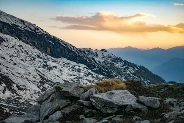 Snow-covered mountains at sunset with a rocky foreground, showcasing n